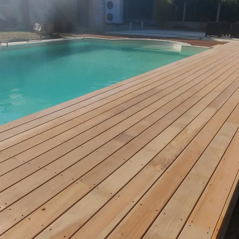 Terrasse en lames de bois blondes autour d'une table ronde, vues depuis un angle montrant le grain du bois et la jonction avec un petit jardin planté